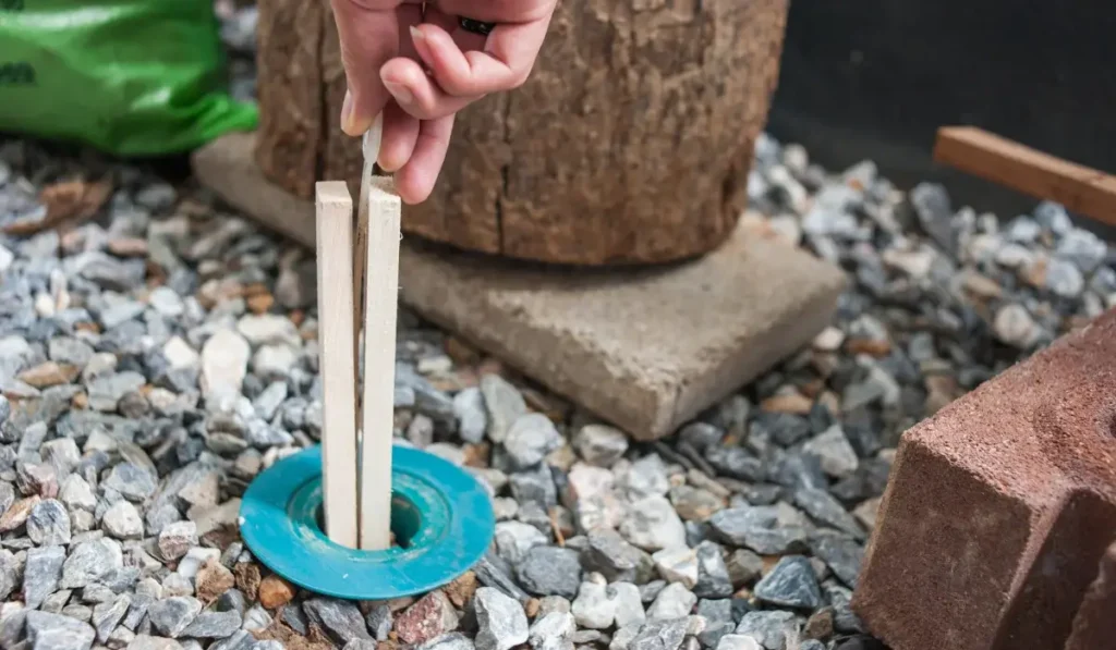 A hand pulls termite baiting sticks from a blue container among rocks and bricks, protecting homes in Charlotte NC.