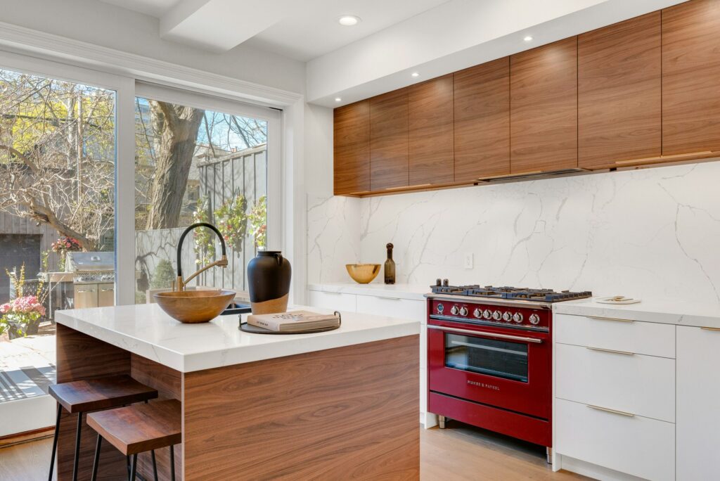 Modern kitchen with wood cabinets, red stove, and garden views—ideal space to protect home from pests this spring.