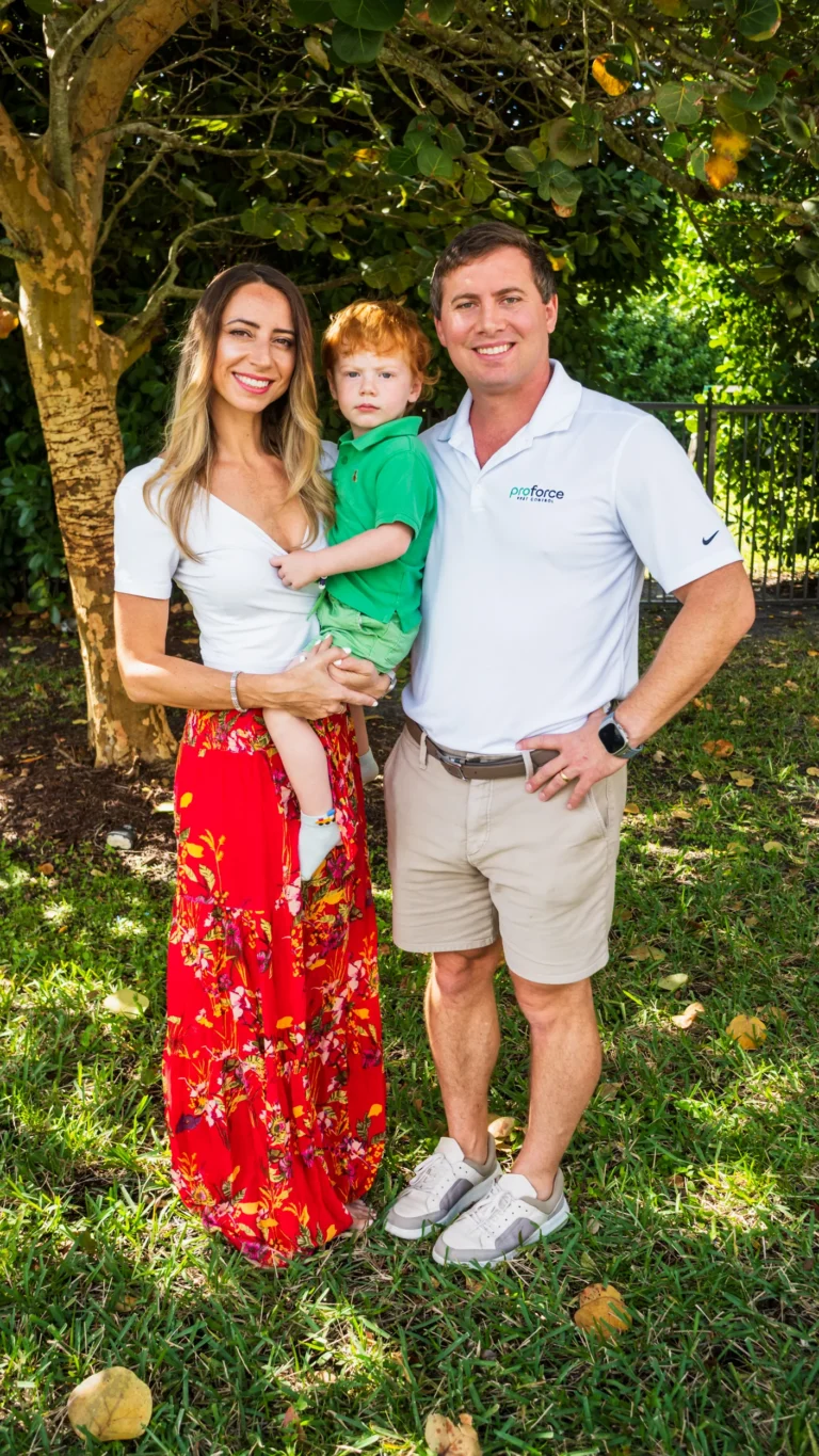 A smiling woman, man, and young boy pose together outdoors under a tree with a Service Template on a sunny day.