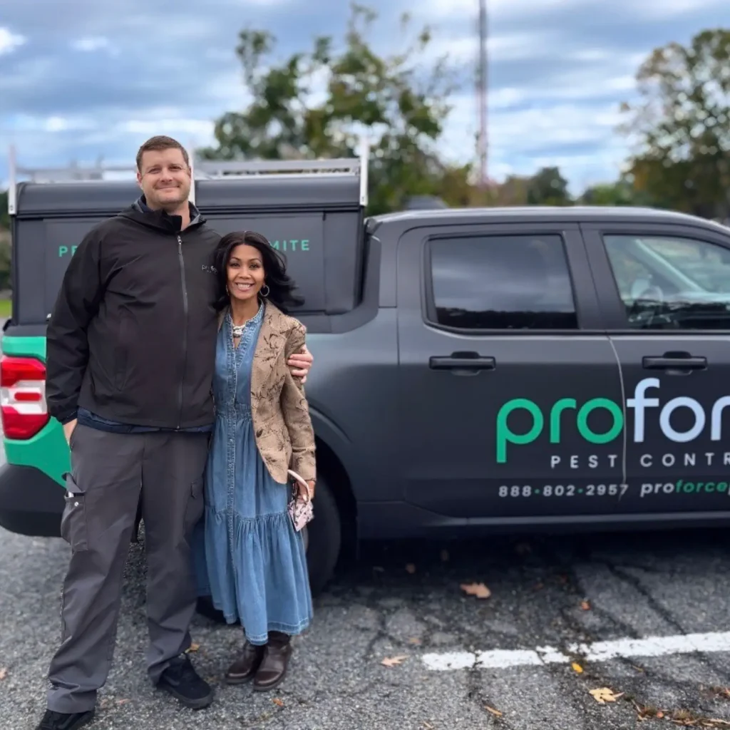 A smiling man and woman stand together in front of a Proforce Pest Control truck, showing Proforce Cares for stronger communities.