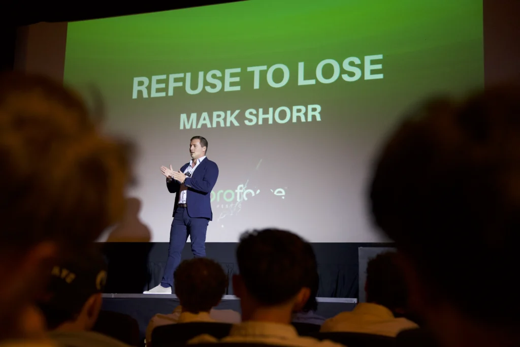 Mark Shorr, Proforce CEO, stands on stage in front of a screen reading REFUSE TO LOSE MARK SHORR with an audience watching.